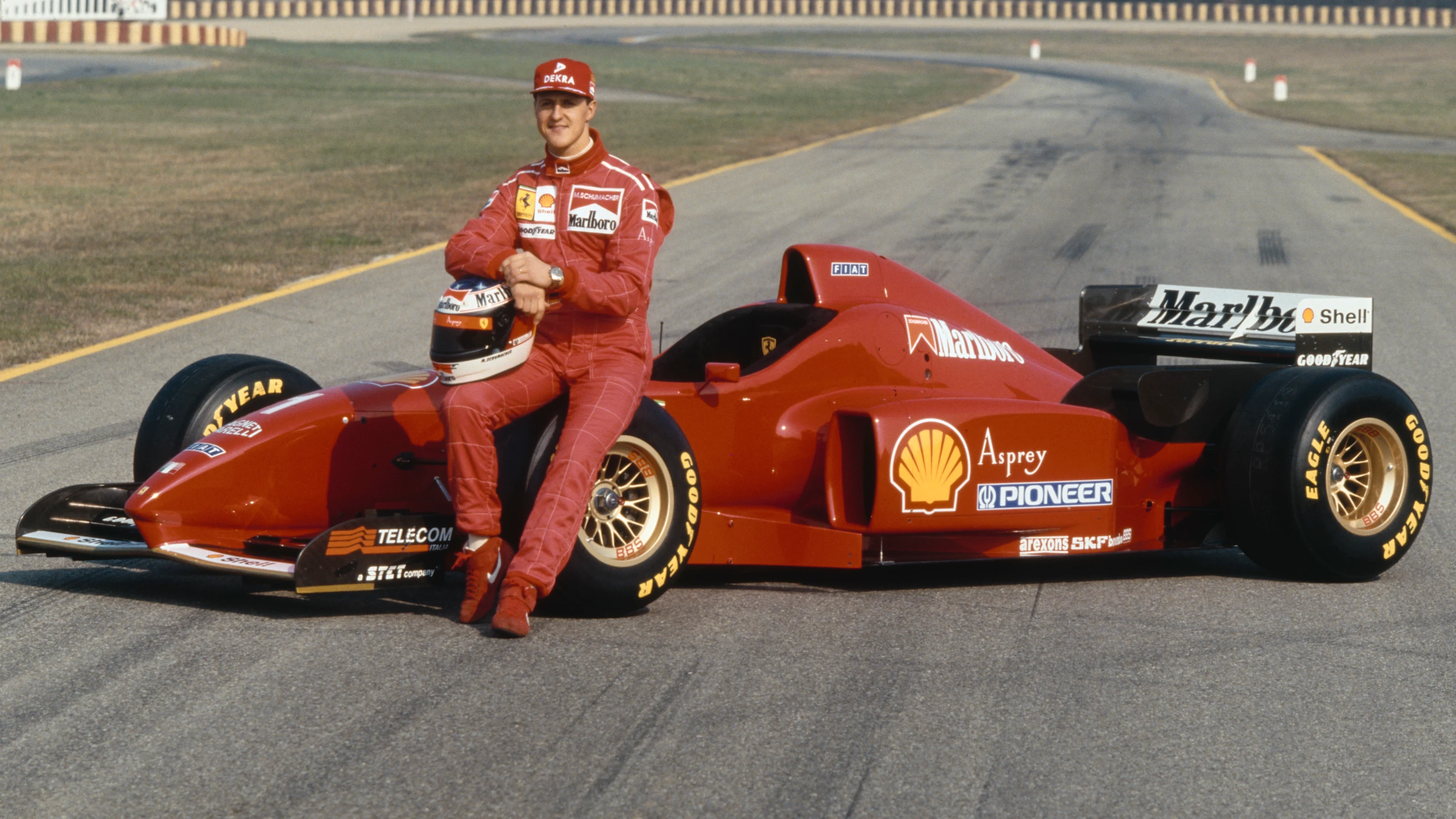 German racing driver Michael Schumacher poses with his crash helmet as he sits on the Ferrari F310
