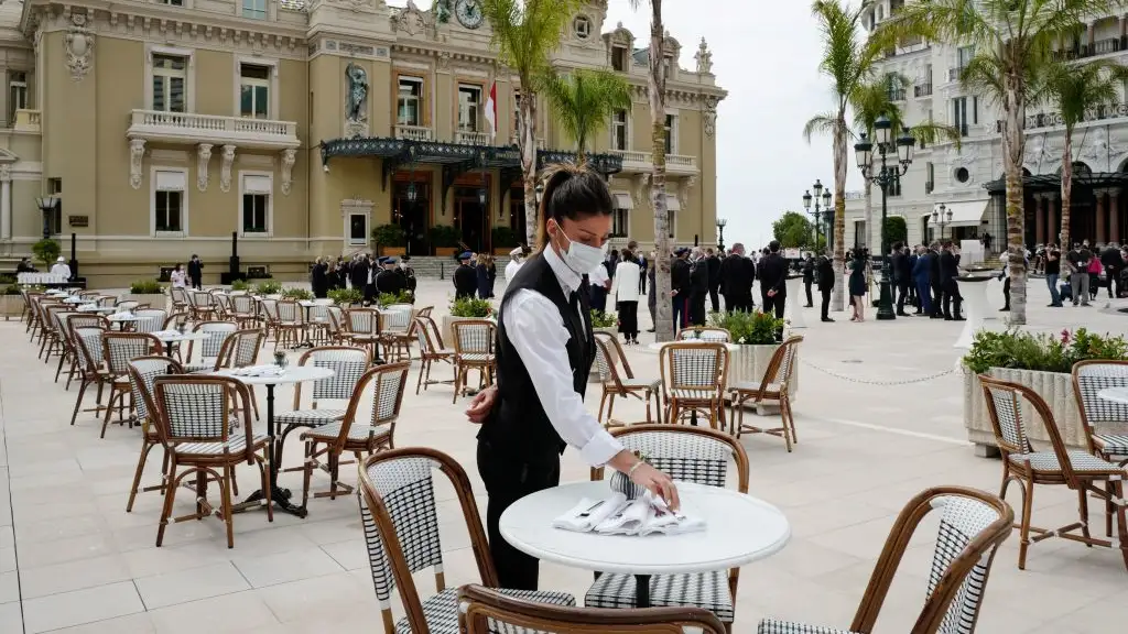 TOPSHOT - A waiter wearing a protective facemask sets a table on the terrace at the Cafe de Paris