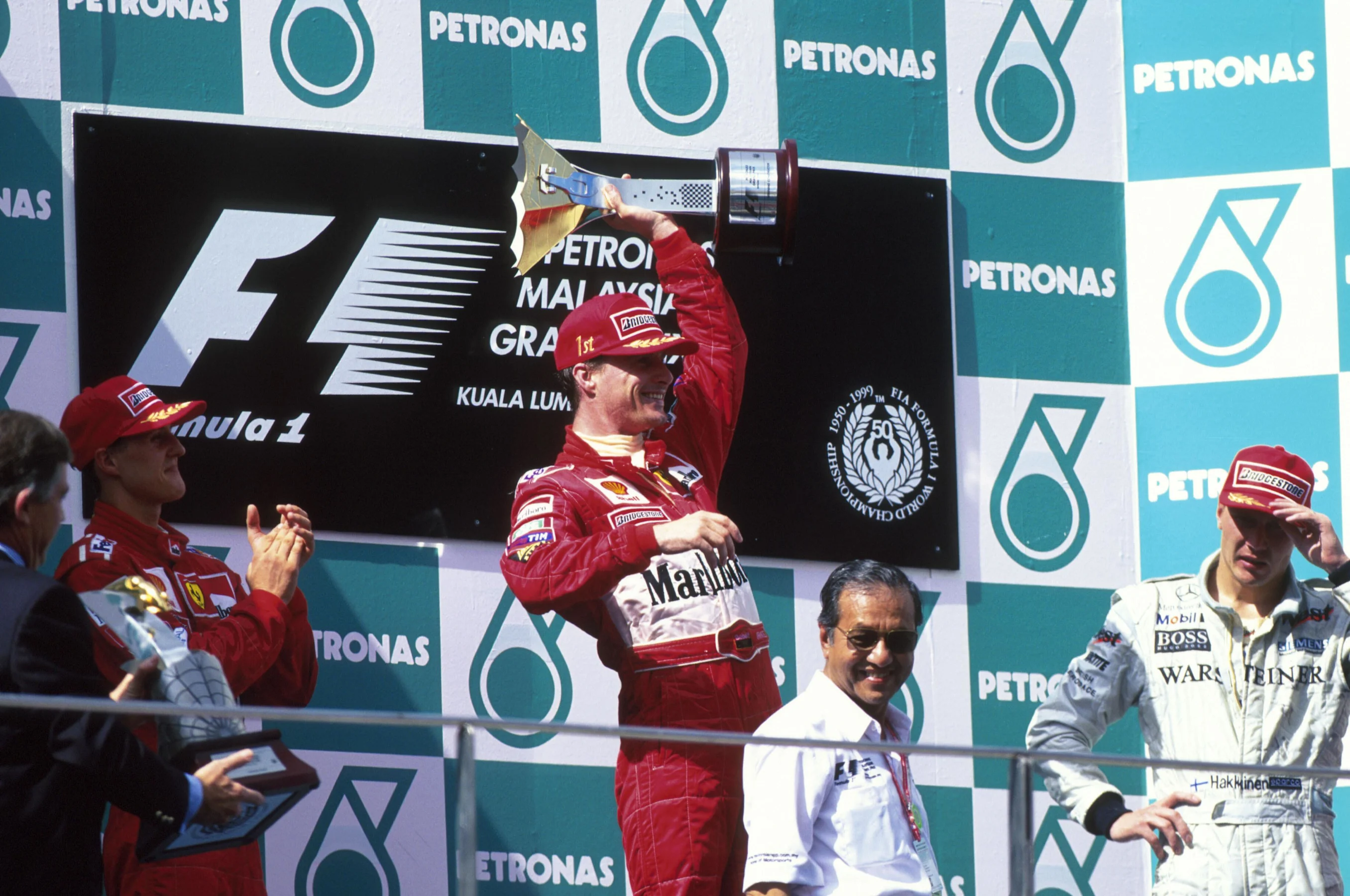 Winner Eddie Irvine celebrates as Schumacher(left) and Hakkinen watch  Malaysian GP, Sepang, 17