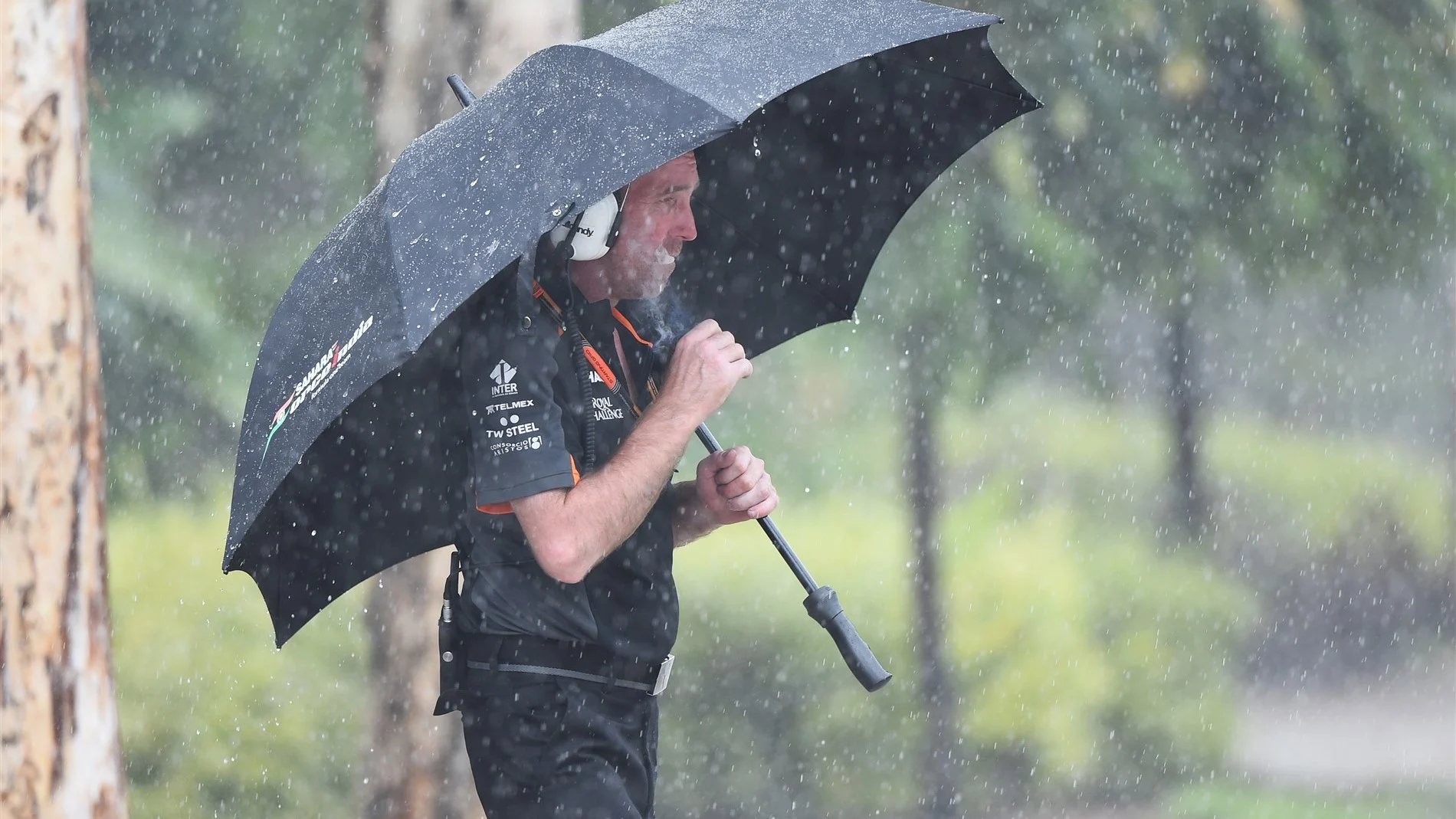 Force India mechanic with Action umbrella in the rain smoking a cigarette at Formula One World