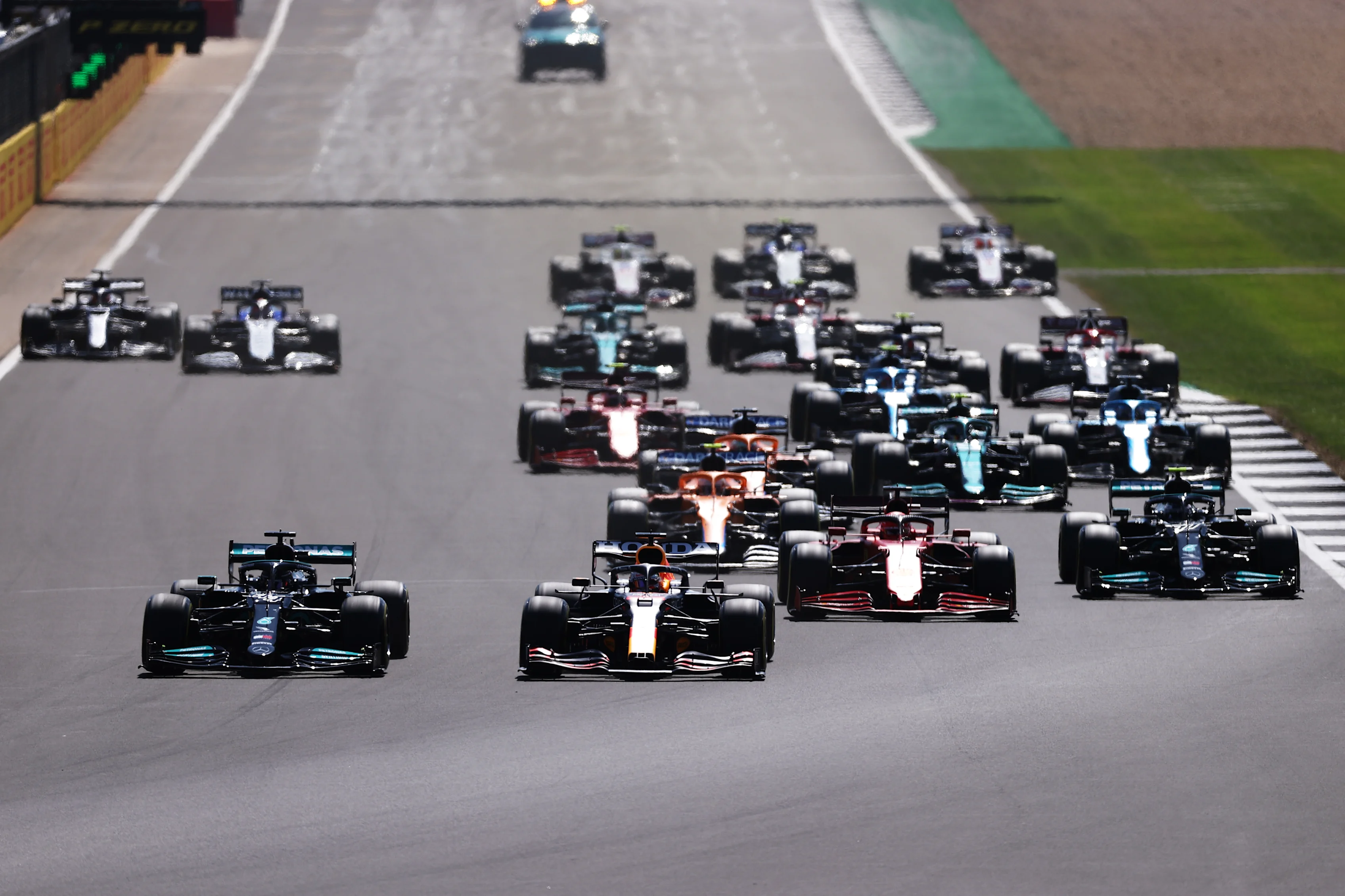 NORTHAMPTON, ENGLAND - JULY 18: Lewis Hamilton of Great Britain driving the (44) Mercedes AMG Petronas F1 Team Mercedes W12 and Max Verstappen of the Netherlands driving the (33) Red Bull Racing RB16B Honda lead the field into turn one at the start during the F1 Grand Prix of Great Britain at Silverstone on July 18, 2021 in Northampton, England. (Photo by Lars Baron/Getty Images)