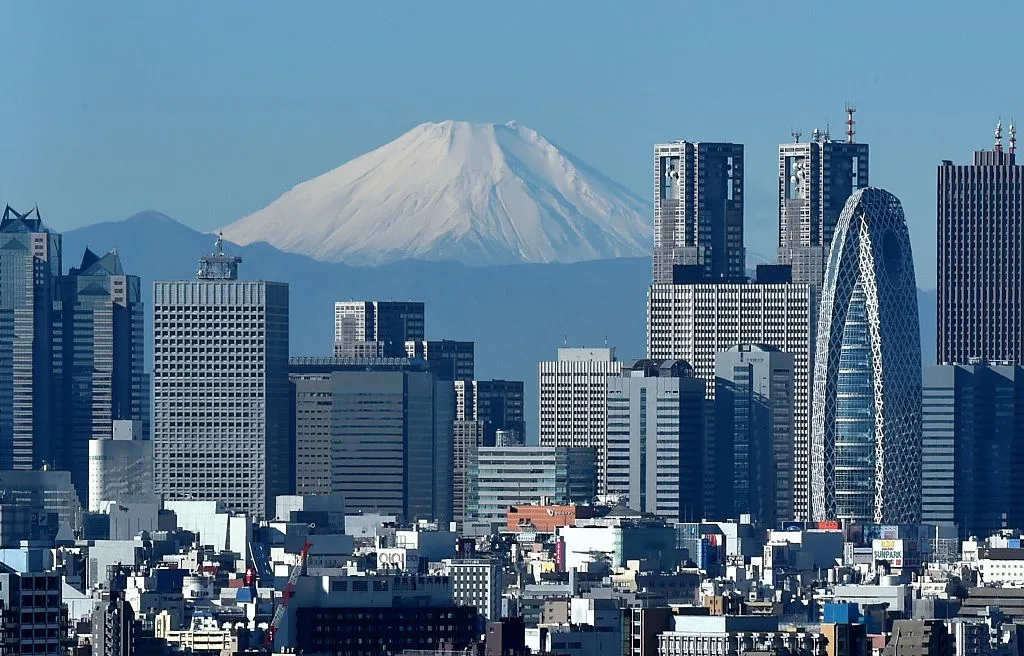 Japan's highest mountain, Mount Fuji (C) is seen behind the skyline of the Shinjuku area of Tokyo