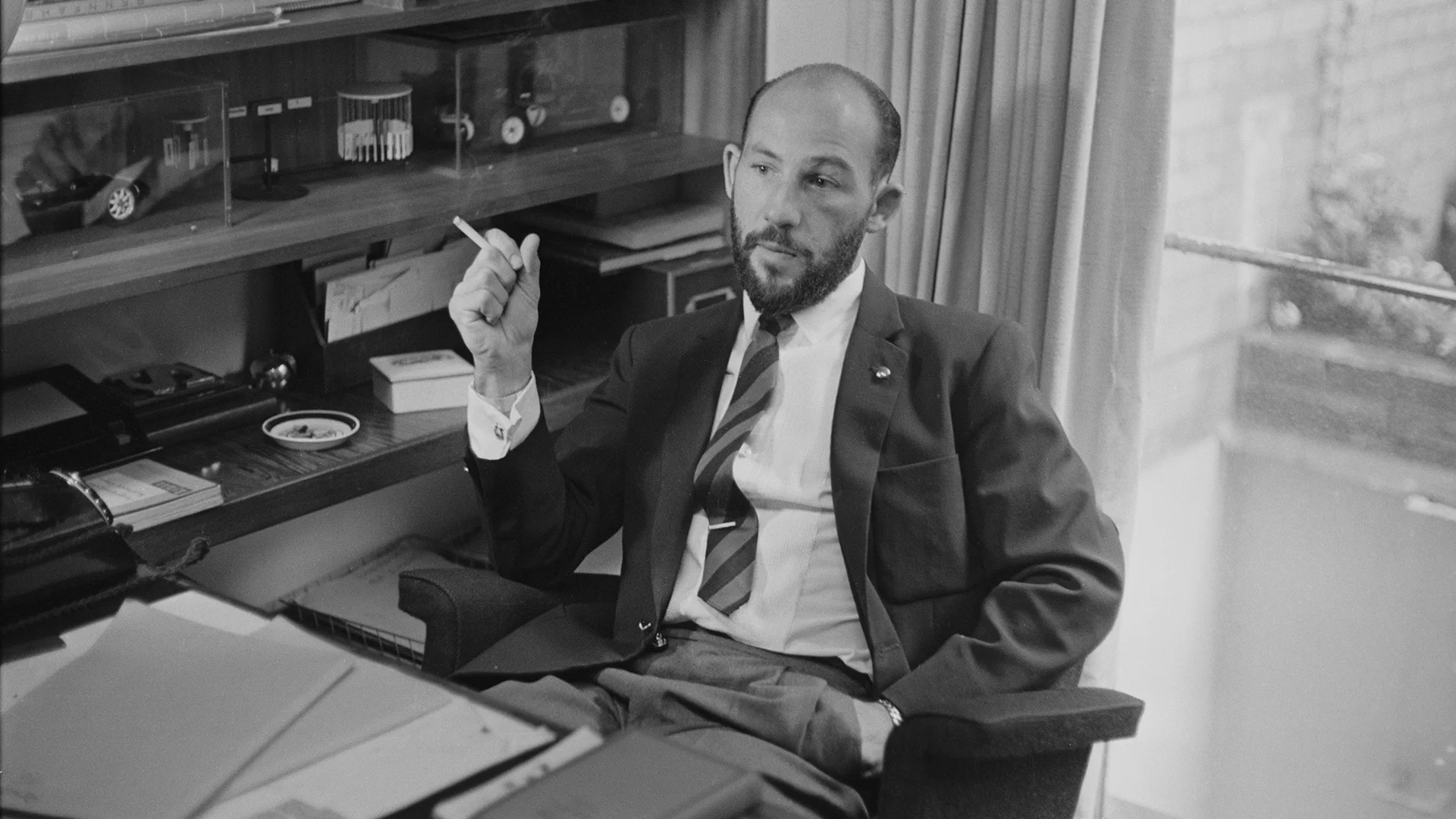 British former Formula One racing driver Stirling Moss pictured smoking a cigarette whilst seated