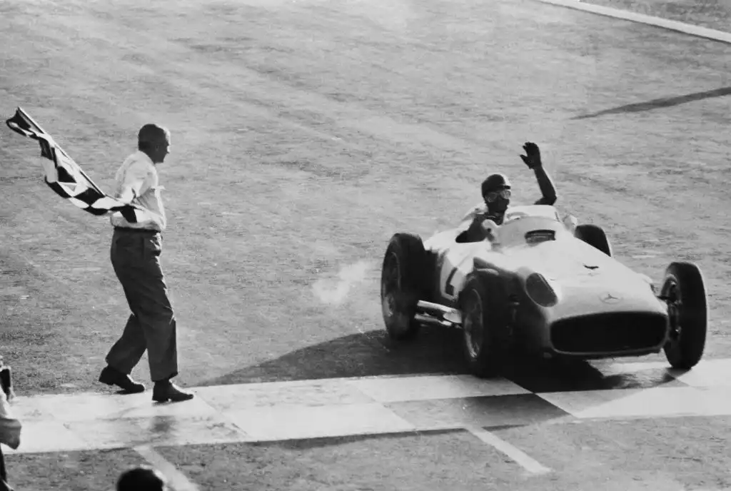 TOPSHOT - Argentine driver Juan Manuel Fangio, steering his Mercedes, salutes as he crosses the