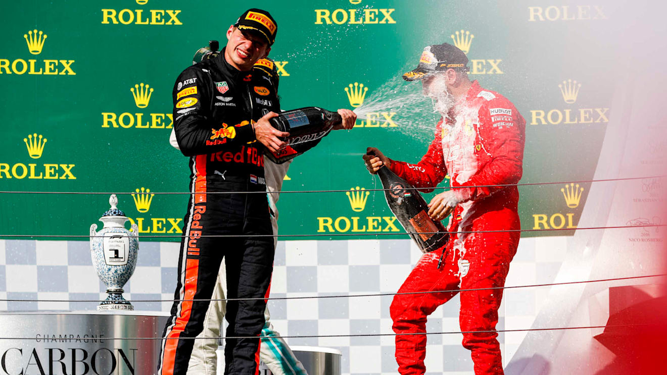 HUNGARORING, HUNGARY - AUGUST 04: Max Verstappen, Red Bull Racing, 2nd position, blasts Sebastian Vettel, Ferrari, 3rd position, with Champagne during the Hungarian GP at Hungaroring on August 04, 2019 in Hungaroring, Hungary. (Photo by Zak Mauger / LAT Images)