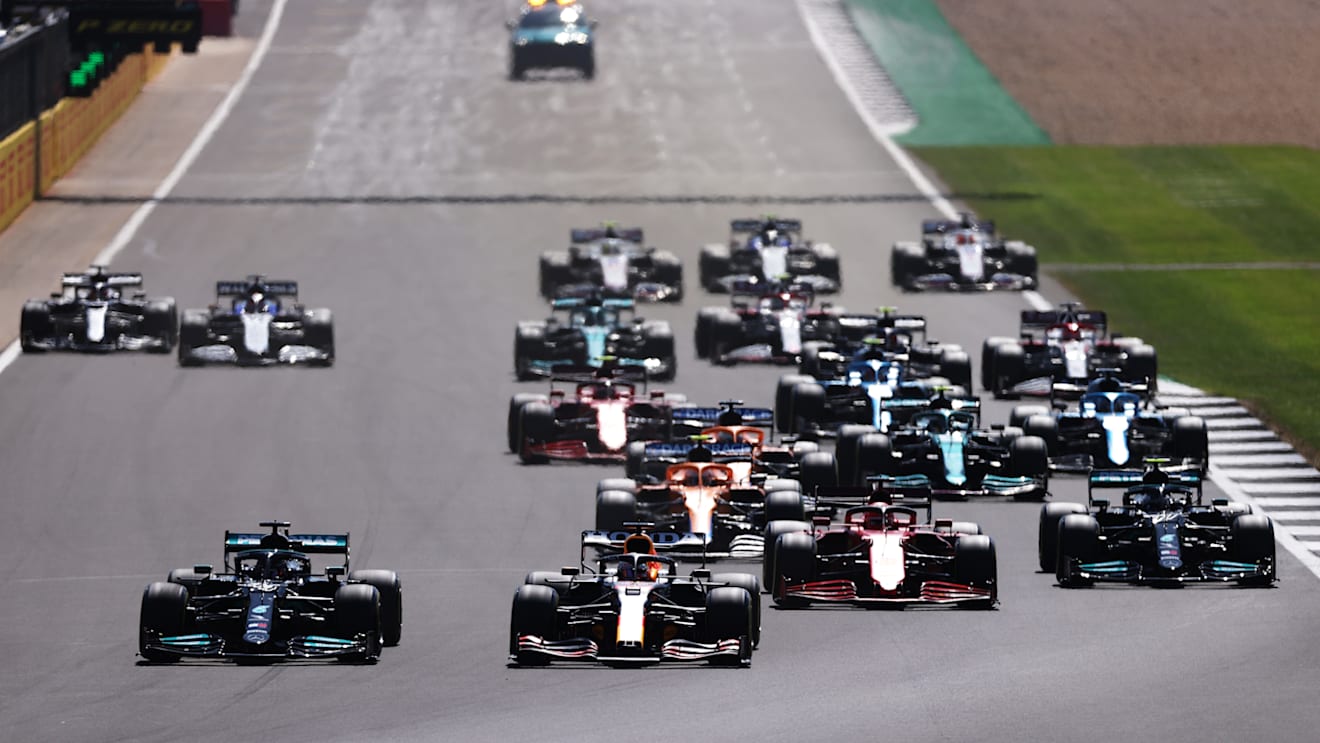 NORTHAMPTON, ENGLAND - JULY 18: Lewis Hamilton of Great Britain driving the (44) Mercedes AMG Petronas F1 Team Mercedes W12 and Max Verstappen of the Netherlands driving the (33) Red Bull Racing RB16B Honda lead the field into turn one at the start during the F1 Grand Prix of Great Britain at Silverstone on July 18, 2021 in Northampton, England. (Photo by Lars Baron/Getty Images)