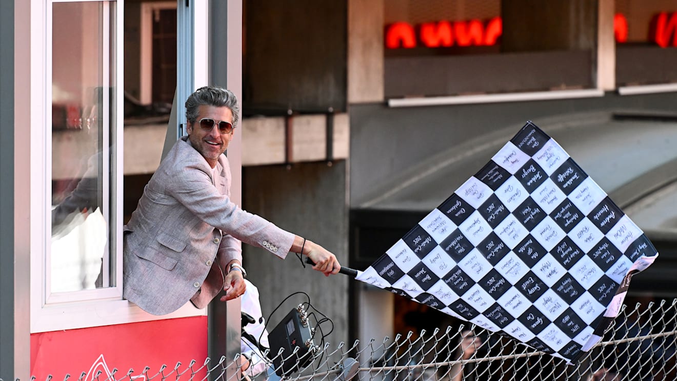 Patrick Dempsey waves the chequered flag at the end of the Grand Prix
