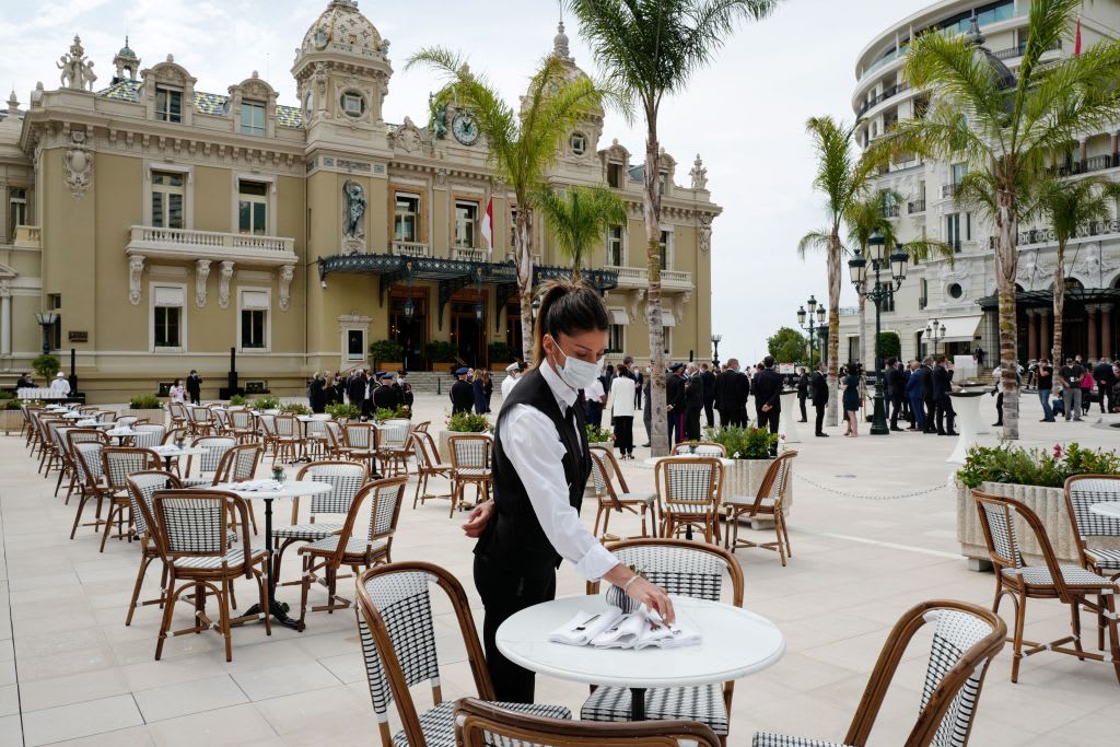 TOPSHOT - A waiter wearing a protective facemask sets a table on the terrace at the Cafe de Paris