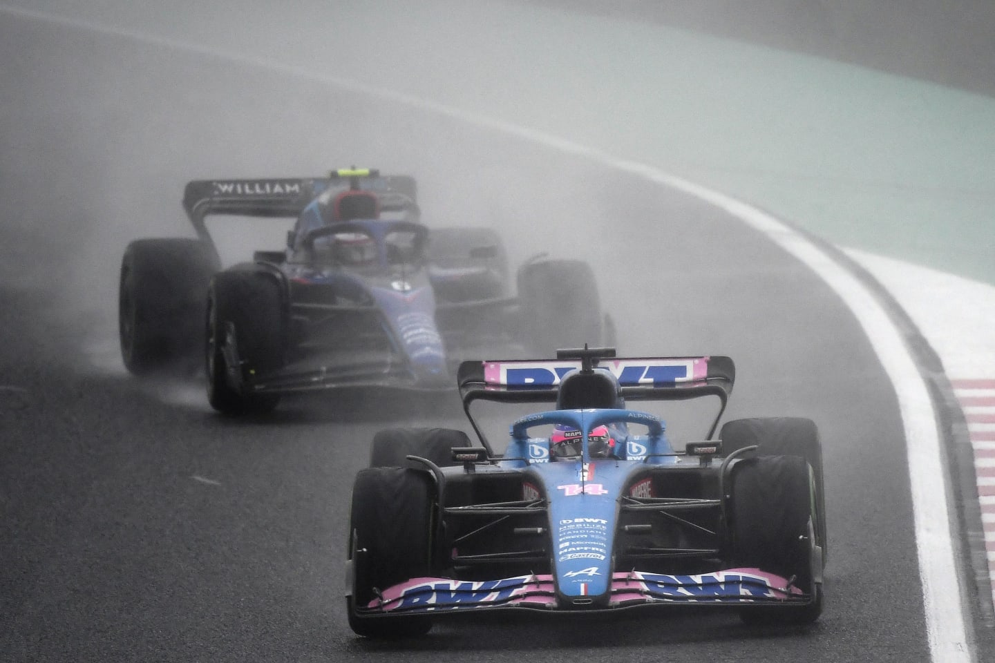 Alpine's Spanish driver Fernando Alonso (C) drives in front of Williams' Canadian driver Nicholas Latifi during the Formula One Japanese Grand Prix at Suzuka, Mie prefecture on October 9, 2022. (Photo by Toshifumi KITAMURA / AFP) (Photo by TOSHIFUMI KITAMURA/AFP via Getty Images)