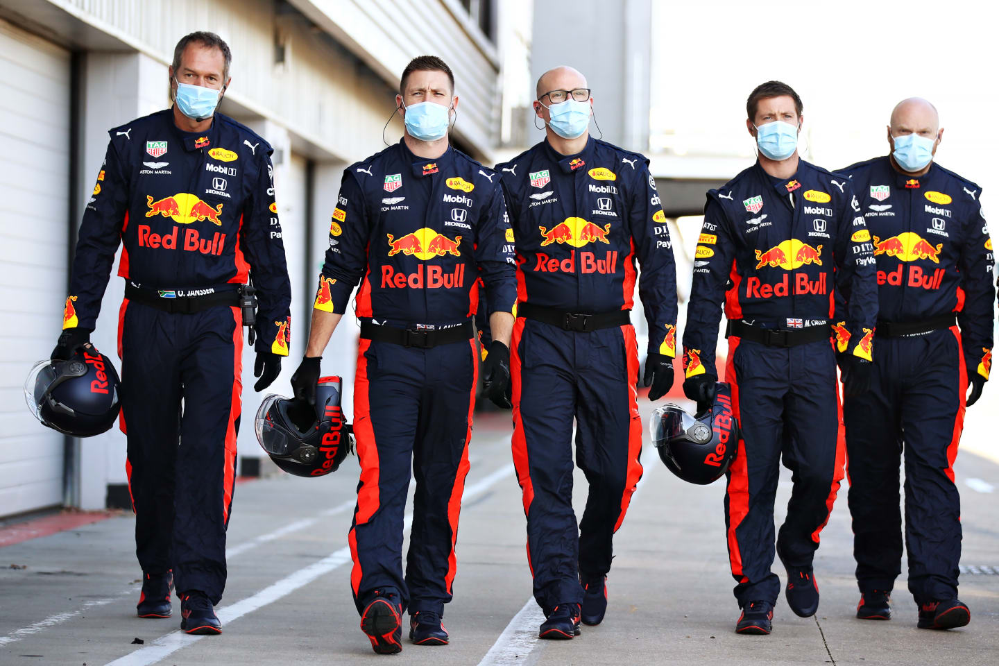 Red Bull mechanics and team personnel walk down the pitlane donning PPE