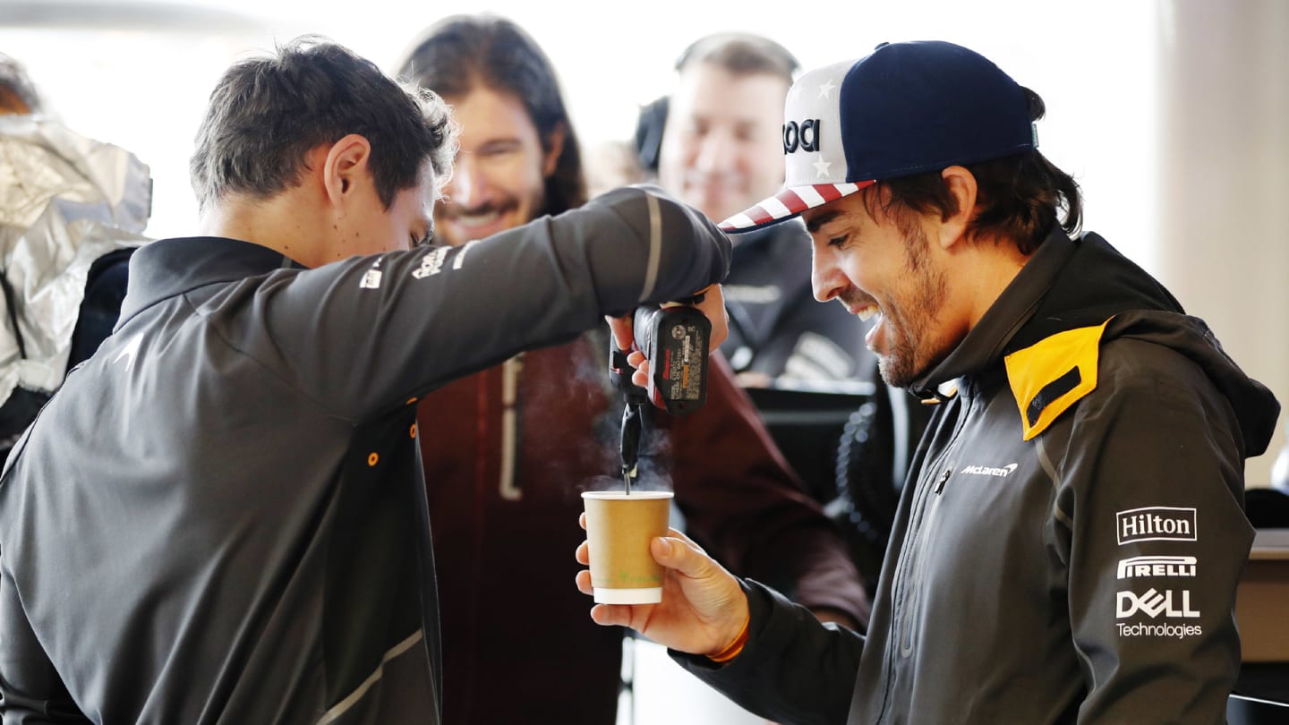 CIRCUIT OF THE AMERICAS, UNITED STATES OF AMERICA - OCTOBER 19: Lando Norris, McLaren, stirs a cup of tea with a power tool for Fernando Alonso, McLaren, as IndyCar driver JR Hildebrand watches in the garage during the United States GP at Circuit of the Americas on October 19, 2018 in Circuit of the Americas, United States of America. (Photo by Steven Tee / LAT Images)