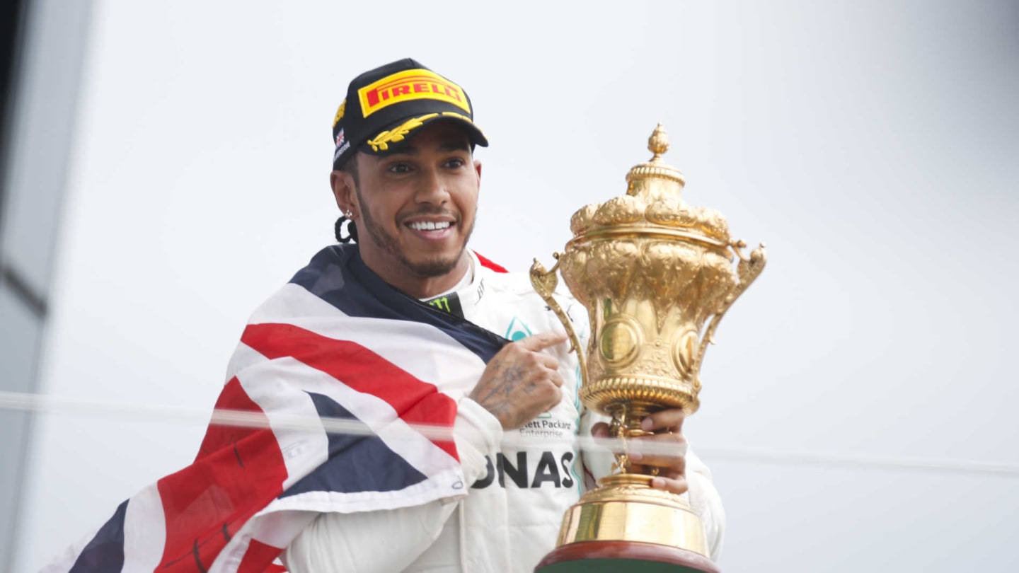 SILVERSTONE, UNITED KINGDOM - JULY 14: Race winner Lewis Hamilton, Mercedes AMG F1 celebrates on the podium with the trophy and with a flag during the British GP at Silverstone on July 14, 2019 in Silverstone, United Kingdom. (Photo by Joe Portlock / LAT Images)