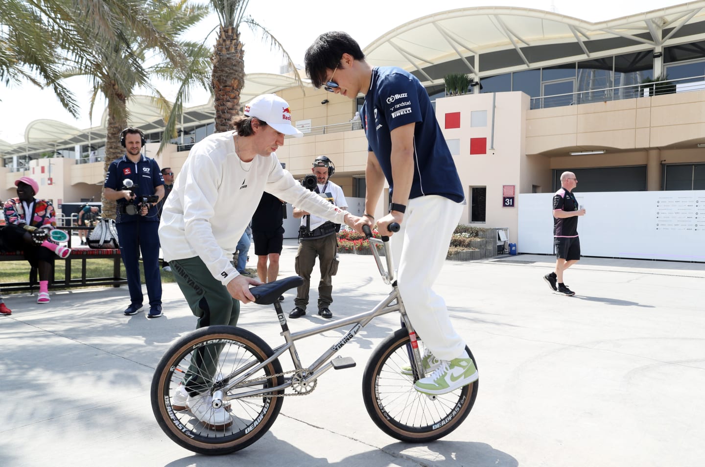BAHRAIN, BAHRAIN - MARCH 04: Yuki Tsunoda of Japan and Scuderia AlphaTauri and Viki Gomez practice bicycle tricks in the Paddock prior to final practice ahead of the F1 Grand Prix of Bahrain at Bahrain International Circuit on March 04, 2023 in Bahrain, Bahrain. (Photo by Peter Fox/Getty Images)