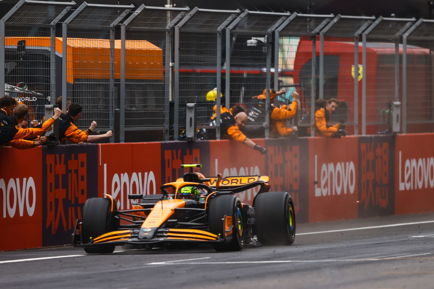 Team members of McLaren celebrate while hanging from the pit wall, as Lando Norris, McLaren MCL38,