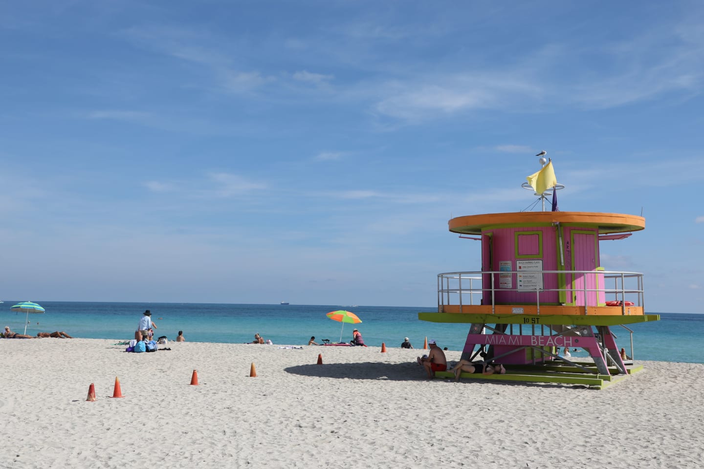People sit in the shade of a lifeguard tower on the beach in the Art Deco Historic District in