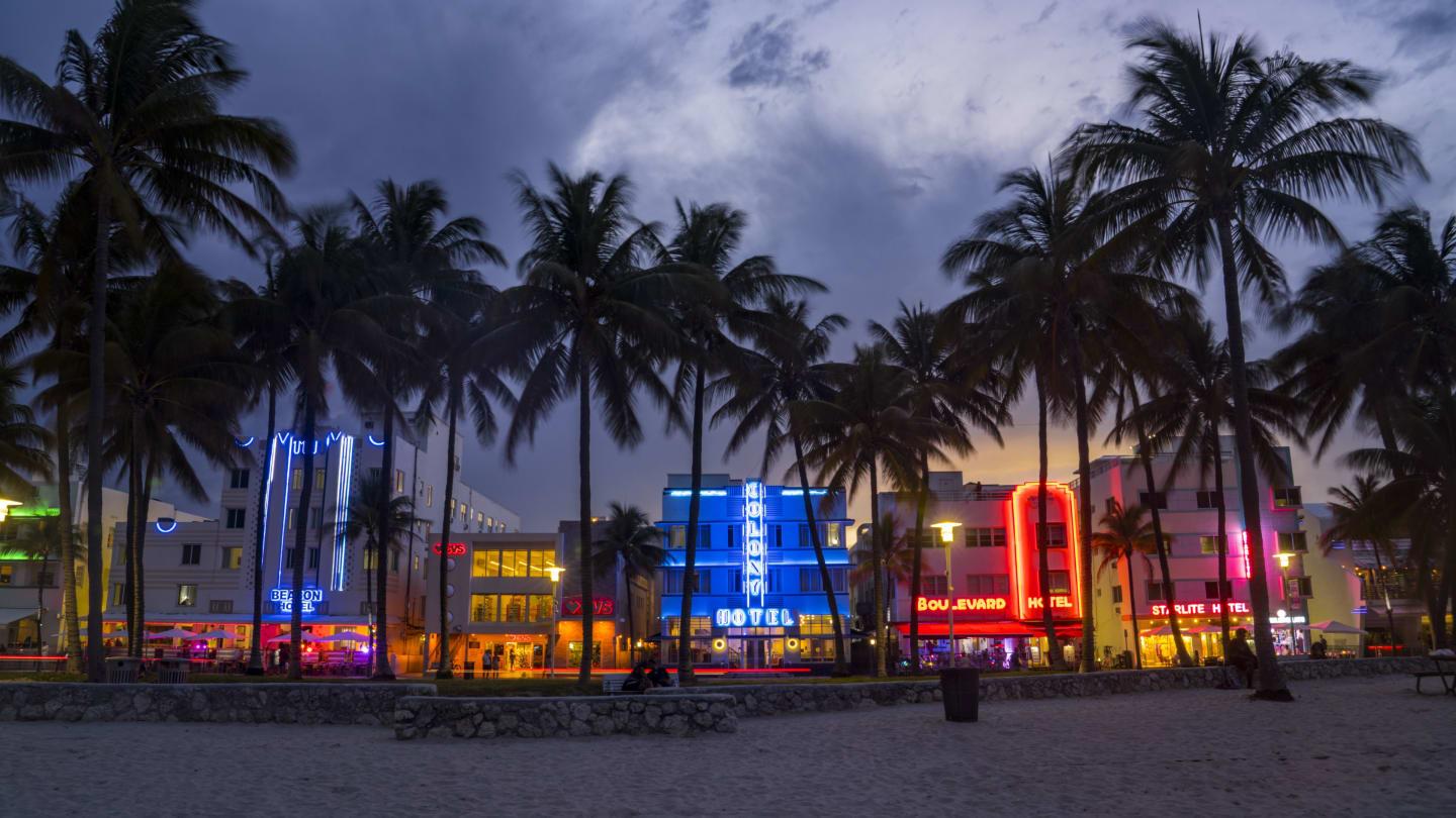 Art Deco District, Miami Beach shows colorful retro neon signs with palm trees and clouds on beach,