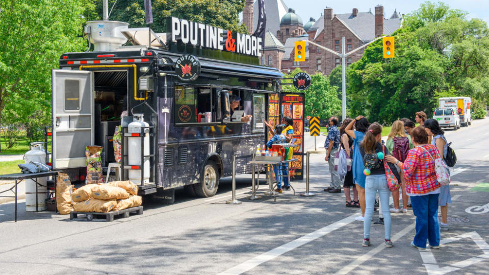 TORONTO, ONTARIO, CANADA - 2022/06/11: A group of people lining-up in a food truck selling Poutine