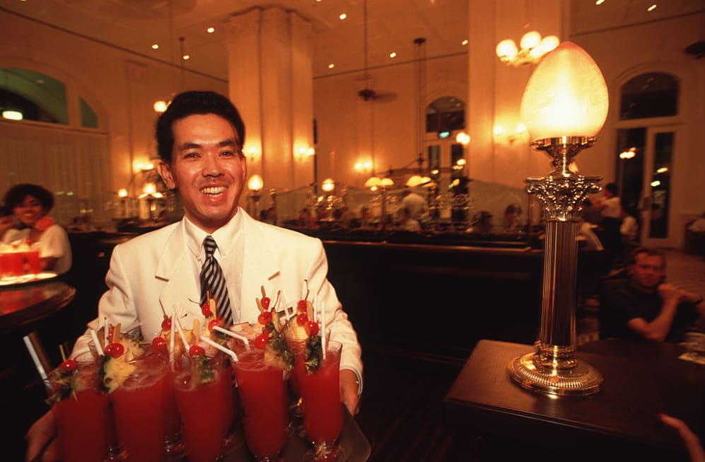 SINGAPORE - 1991/09/01: A waiter carries a tray of "Singapore Slings" in the main bar/pub of the