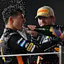 ABU DHABI, UNITED ARAB EMIRATES - DECEMBER 07: Race winner Max Verstappen of the Netherlands and Oracle Red Bull Racing and 2025 F1 World Drivers Champion and Third placed Lando Norris of Great Britain and McLaren celebrate on the podium with Champagne during the F1 Grand Prix of Abu Dhabi at Yas Marina Circuit on December 07, 2025 in Abu Dhabi, United Arab Emirates. (Photo by Clive Mason/Getty Images)