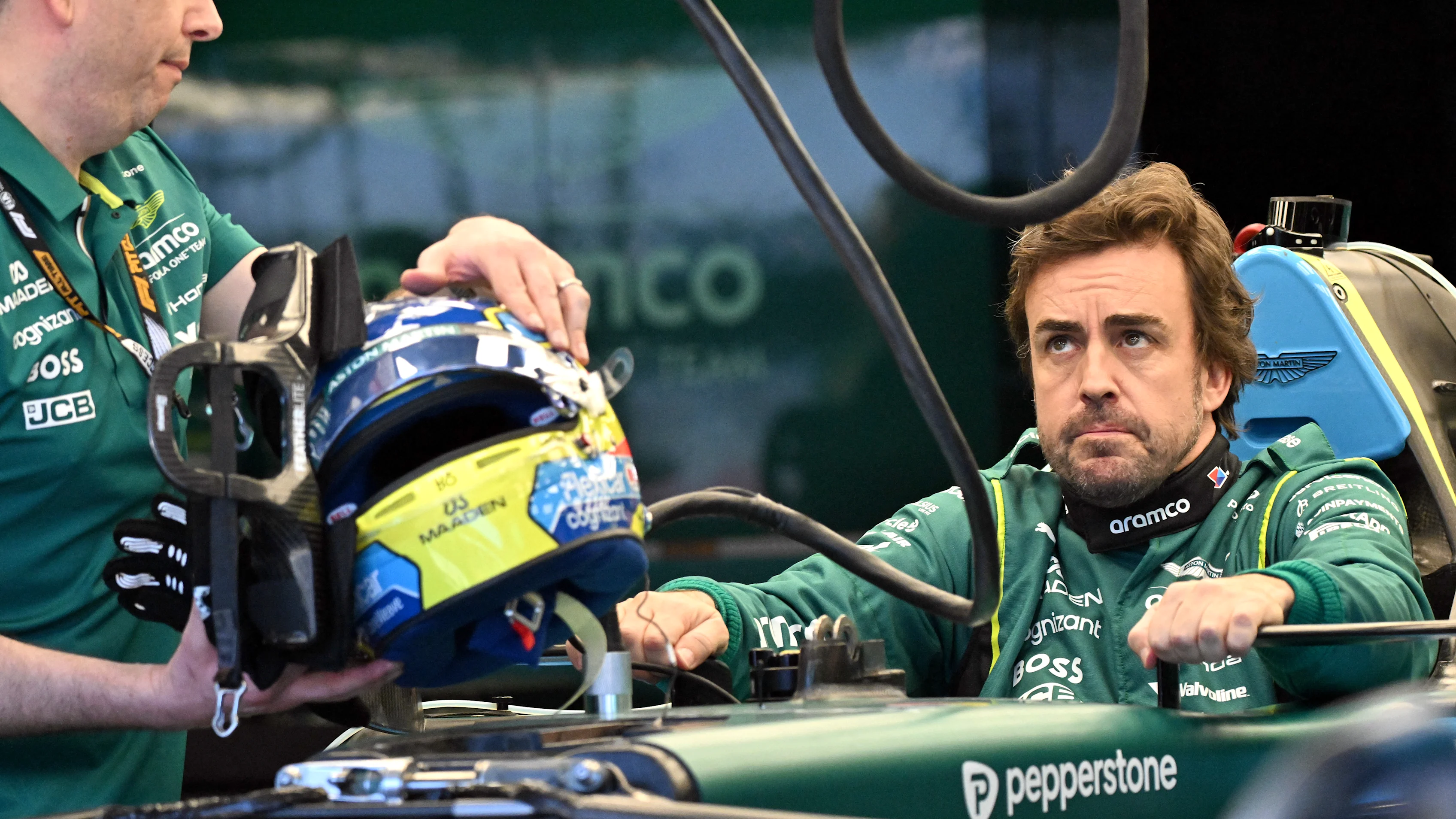 Aston Martin's Spanish driver Fernando Alonso inspects his car with team mechanics in the garage