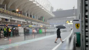 A man walks under the rain at the pit lane before the qualifying session for the upcoming Formula