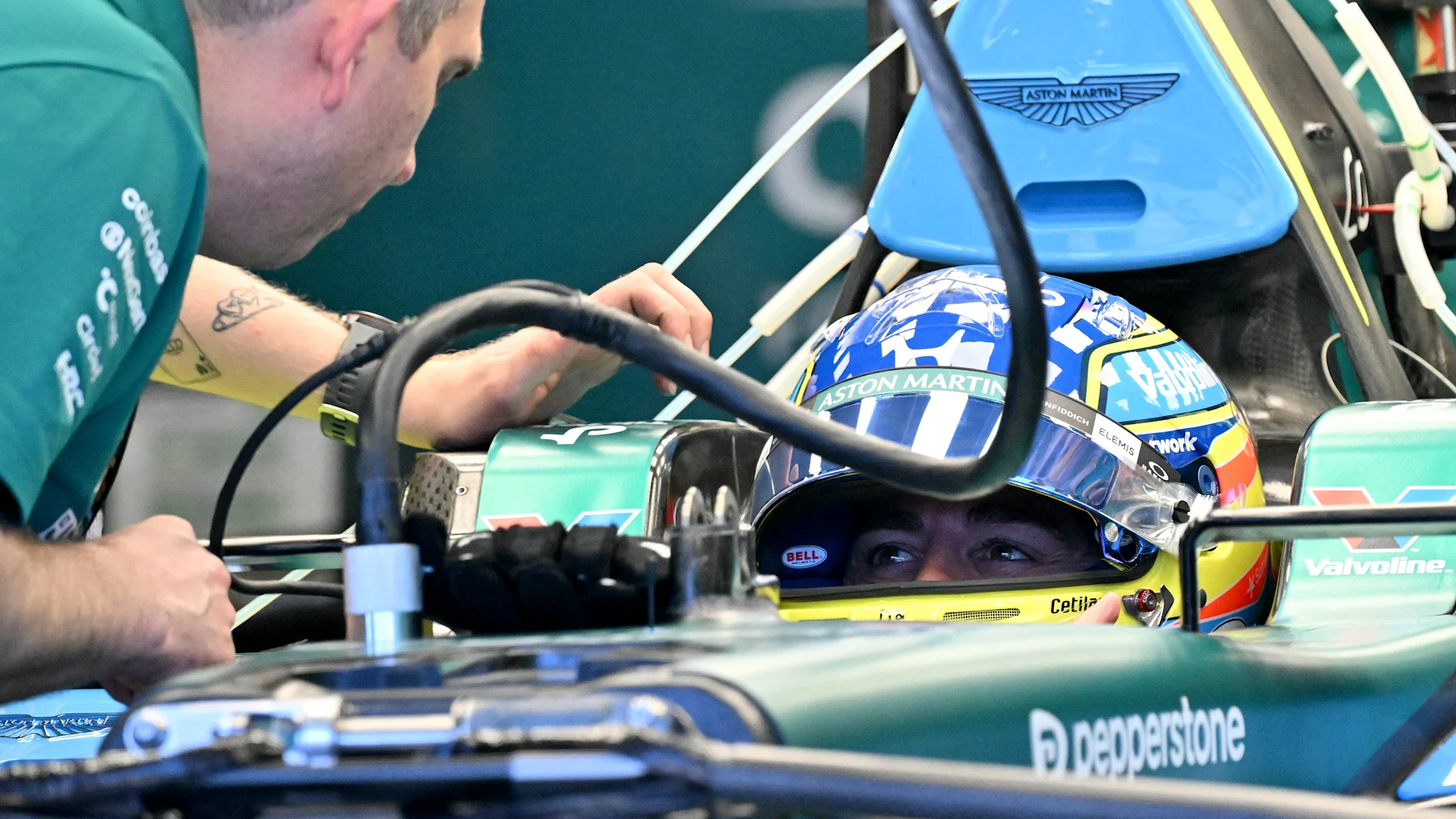 Aston Martin's Spanish driver Fernando Alonso inspects his car with team mechanics in the garage