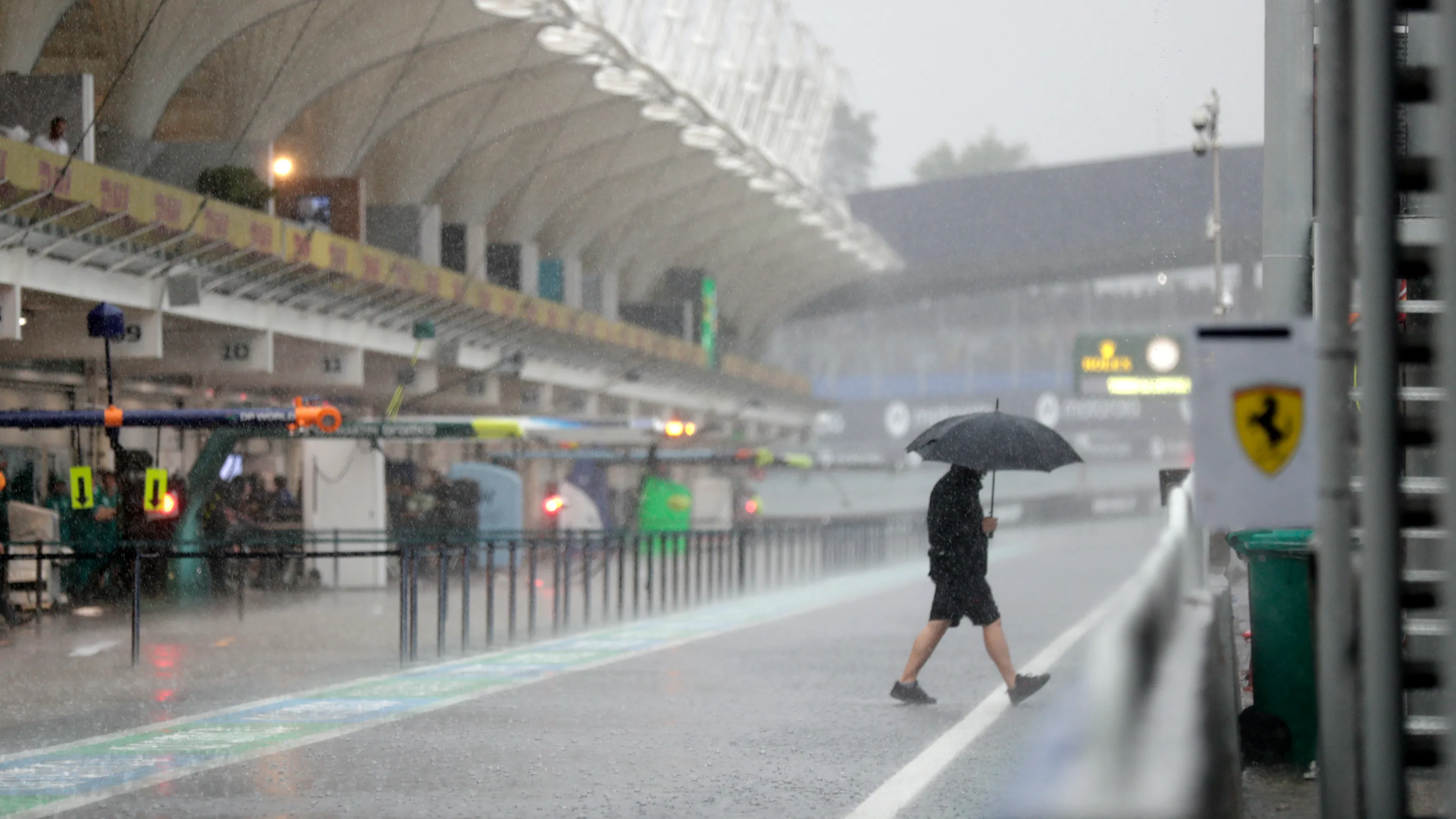 A man walks under the rain at the pit lane before the qualifying session for the upcoming Formula