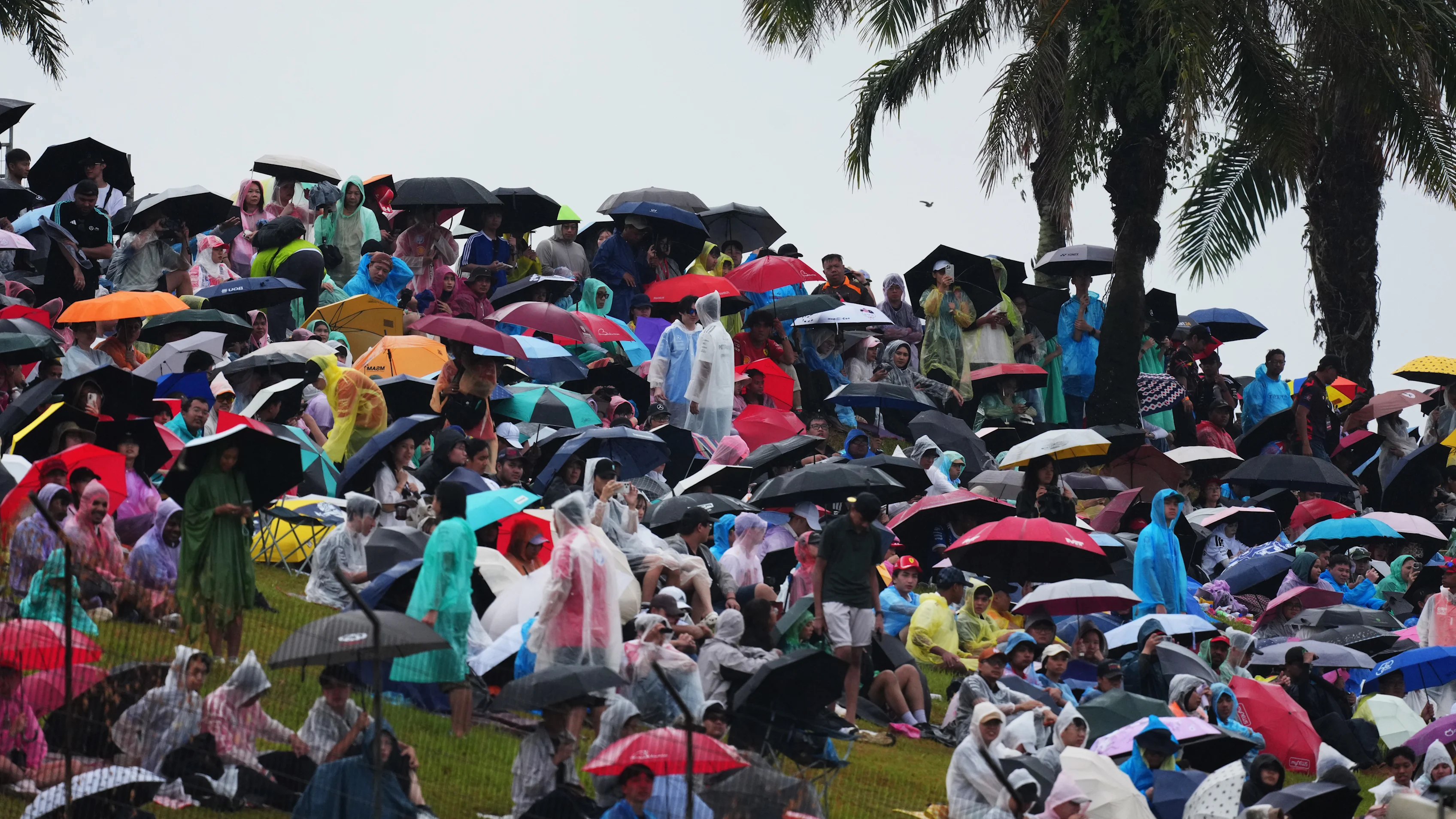 KUALA LUMPUR, MALAYSIA - OCTOBER 04: Fans shelter underneath umbrellas as they look on from a